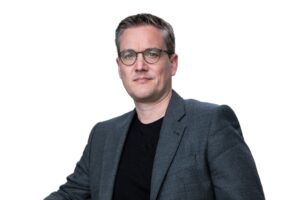 Sebastian Bluhm Portraitbild mit grauem Sakko und schwarzen T-Shirt freigestellt