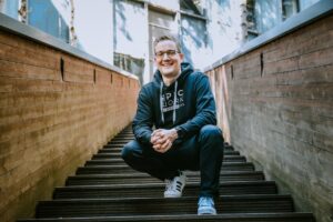 Sebastian Bluhm knieend auf einer Treppe im Hoodie