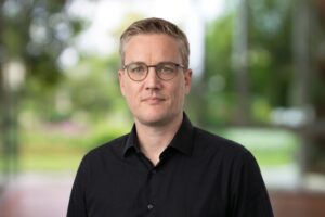 Sebastian Bluhm Portraitbild mit schwarzem Hemd vor einem grünen Hintergrund