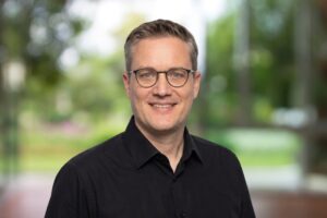 Sebastian Bluhm Portraitbild mit schwarzem Hemd vor einem grünen Hintergrund