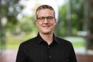 Sebastian Bluhm Portraitbild mit schwarzem Hemd vor einem grünen Hintergrund